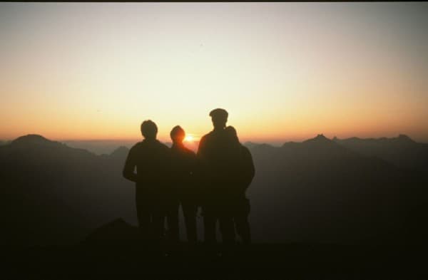 Drei Personen als Silhouette vor Bergen bei Sonnenuntergang